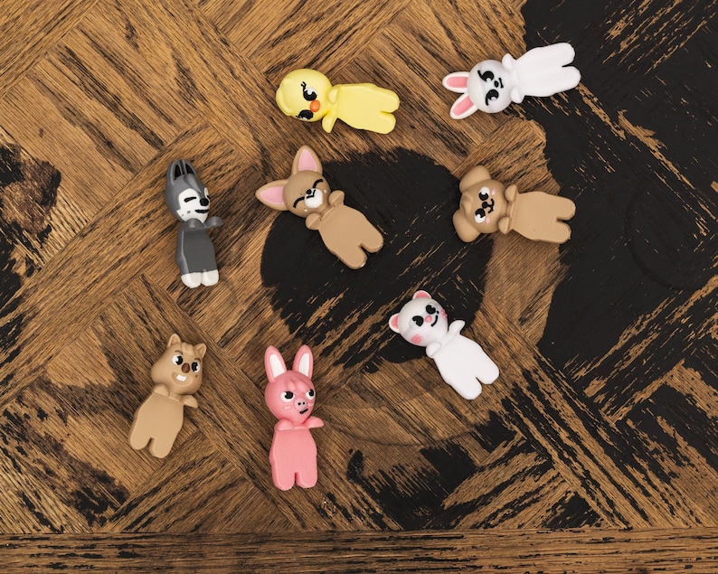 Puede incluir: Una colecci&oacute;n de peque&ntilde;as figuras de animales de colores, que incluyen un pollito amarillo, un conejo blanco, un lobo gris, un oso marr&oacute;n, un conejito rosa y un oso blanco. Las figuras est&aacute;n sobre una superficie de madera.