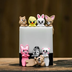 Puede incluir: Un objeto cil&iacute;ndrico blanco y negro adornado con varias peque&ntilde;as figuras de animales de colores. Las figuras incluyen una ardilla, un pollito, un conejo, un zorro, un cerdo, un lobo, un perro y un gato. Los animales est&aacute;n en varias poses.