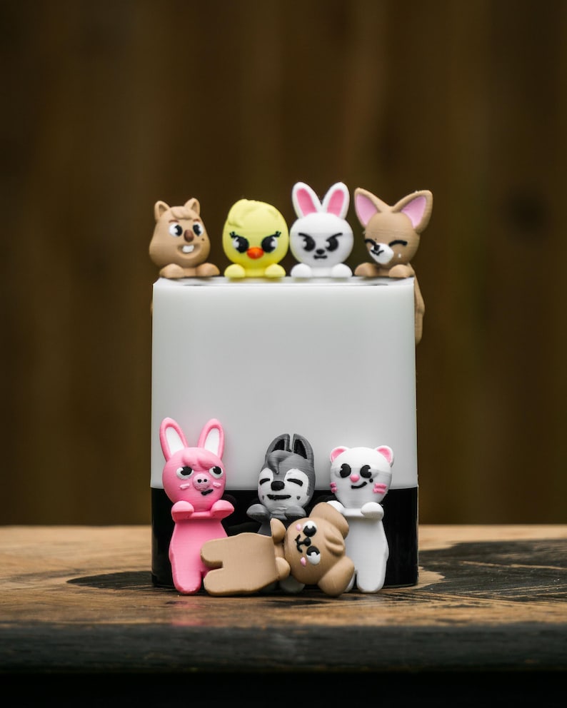 Puede incluir: Un objeto cil&iacute;ndrico blanco y negro adornado con varias peque&ntilde;as figuras de animales de colores. Las figuras incluyen una ardilla, un pollito, un conejo, un zorro, un cerdo, un lobo, un perro y un gato. Los animales est&aacute;n en varias poses.