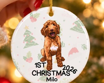 May include: A round white ceramic ornament featuring a brown doodle dog illustration in the center. The text reads 1ST CHRISTMAS 2026 and the name Milo. The background has a light pattern of green Christmas trees and pink holly berries.