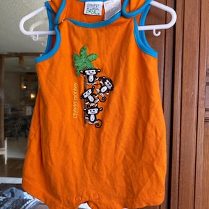 May include: Orange sleeveless baby onesie with a blue trim. The onesie has a graphic of monkeys climbing a palm tree with the text "cheeky monkeys" on the side. The onesie has the brand name "Simply Basic" on the front.