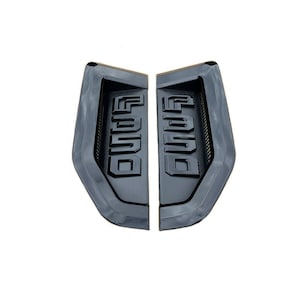 Puede incluir: Un par de emblemas Ford de plástico negro con letras "FORD" en relieve. Los emblemas están diseñados para ser montados en un vehículo.