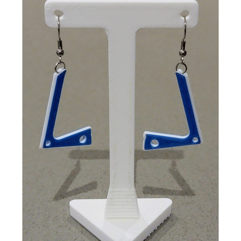 Pu&ograve; includere: Un paio di orecchini geometrici blu e bianchi con ganci d'argento. Gli orecchini hanno la forma di un angolo retto con un piccolo foro al centro dell'angolo.