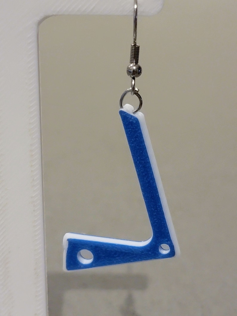 Pu&ograve; includere: Orecchini stampati in 3D blu e bianchi a forma di lettera L. Gli orecchini sono appesi a ganci argentati.