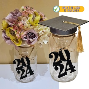 Puede incluir: Dos tarros de cristal con letreros negros que indican el año de graduación 2024. Un tarro tiene un gorro de graduación negro en la parte superior con una borla dorada. Ambos tarros están decorados con cuerda y un ramo de flores artificiales.