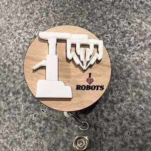 May include: A wooden badge holder with a white 3D robot arm and the text "I ♥ ROBOTS". The badge holder is attached to a retractable badge reel.