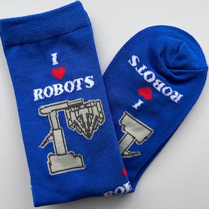 Puede incluir: Un par de calcetines azules con un diseño de robot blanco y el texto "Me encantan los robots".