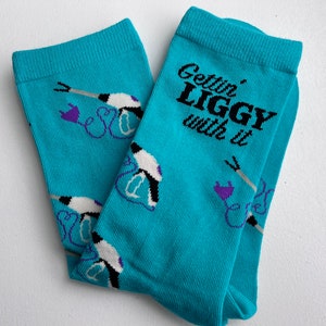 May include: A pair of turquoise blue socks with a white and purple design. The socks have the text "Gettin' Liggy with it" printed on them.