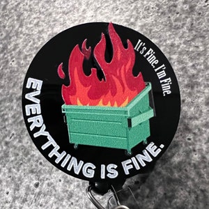 May include: A black badge reel with the phrase "Everything is Fine" in white text. The design features a green dumpster on fire with red and orange flames. The phrase "It's Fine, I'm Fine" is also in white text.