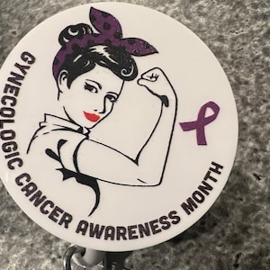 Może przedstawiać: Biała okrągła odznaka z fioletową wstążką i tekstem "GYNECOLOGIC CANCER AWARENESS MONTH". Rysunkowa postać kobiety z fioletowymi włosami w kropki, z uniesioną ręką w geście "damy radę".