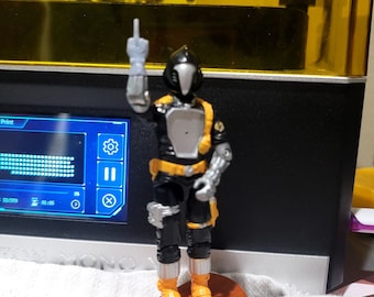 May include: A black and yellow action figure with a helmet and a silver hand, standing on a wooden base. The figure is giving the middle finger.