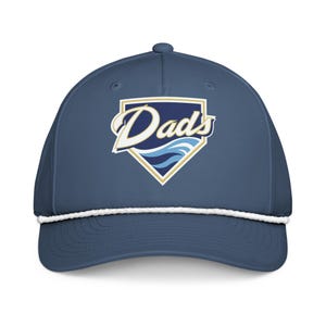 Peut inclure: Casquette de baseball bleu marine avec un détail de corde blanche et une visière incurvée. La casquette affiche le mot "Dads" en écriture blanche dans un écusson bleu marine et or avec des vagues bleues.