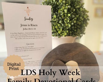 May include: A set of printable LDS Holy Week Family Devotional Cards. The cards feature a brown wooden cutout of a tomb with a white interior, and a white card with the text "Sunday, Jesus is Risen, John 20:11-18".