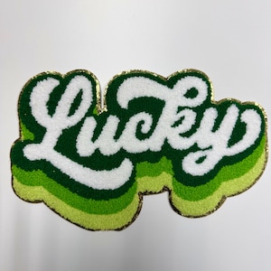 May include: A green and white felt patch with gold trim that says "Lucky" in a retro font.