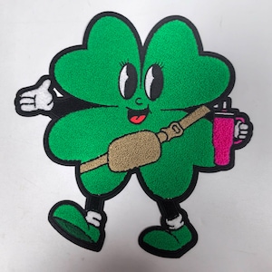 Puede incluir: Un personaje de dibujos animados de trébol de cuatro hojas verde con un cinturón marrón y una botella de agua rosa. El personaje tiene ojos grandes, una lengua roja que sobresale y contornos negros.