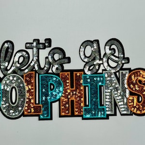 May include: A colorful sequined patch with the text "Let's go Dolphins" in a variety of colors, including turquoise, silver, orange, and brown.