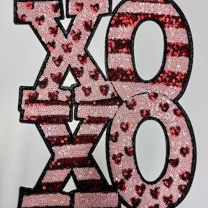 May include: Red and pink sequined iron-on patch with the letters XO in a bold, blocky font.