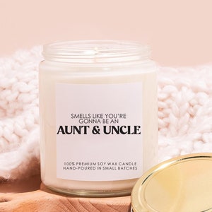 May include: A white soy wax candle in a clear glass jar with a gold lid. The label reads "Smells like you're gonna be an Aunt & Uncle". 100% Premium Soy Wax Candle Hand-Poured in Small Batches.