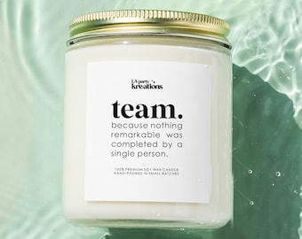 May include: A white soy wax candle with a gold lid. The candle has a label that reads "kreations team. because nothing remarkable was completed by a single person. 100% premium soy wax candle hand poured in small batches".