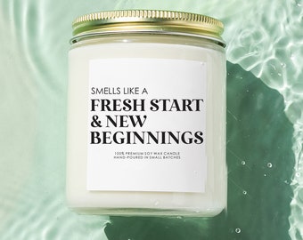 May include: A white soy wax candle with a gold lid. The label reads "Smells like a Fresh Start & New Beginnings" and "100% Premium Soy Wax Candle Hand Poured in Small Batches".