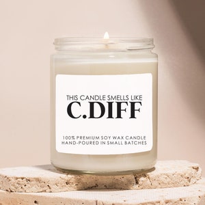 May include: A white candle in a clear glass jar with a black label that reads "THIS CANDLE SMELLS LIKE C.DIFF 100% PREMIUM SOY WAX CANDLE HAND-POURED IN SMALL BATCHES".