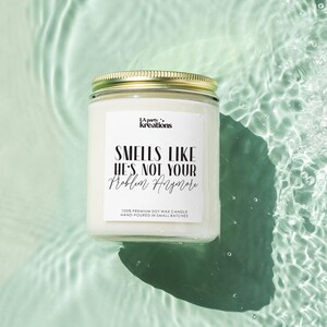 May include: White soy wax candle with a gold lid. The label reads "LA party kreations" and "SMELLS LIKE HE'S NOT YOUR Problem Anymore". The candle is floating in a pool of water.