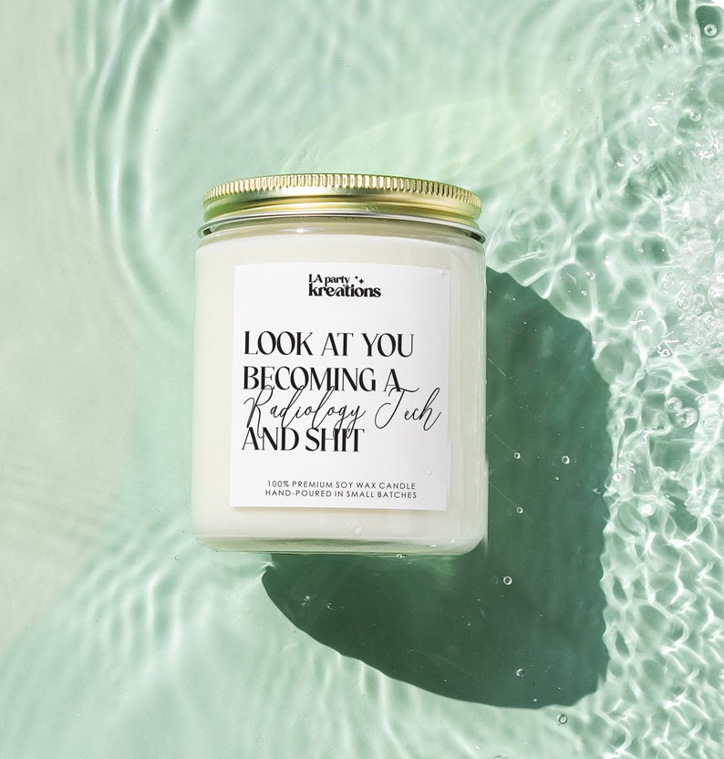 May include: A white soy wax candle with a gold lid. The candle has a black label with the text "LA party+ kreations" and "LOOK AT YOU BECOMING A Radiology Tech AND SHIT". The label also includes the text "100% PREMIUM SOY WAX CANDLE HAND-POURED IN SMALL BATCHES".