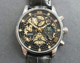 Peut inclure: Une montre à bracelet en cuir noir avec un boîtier argenté et un cadran squelette. La montre a un cadran doré avec des chiffres romains pour les heures et une fenêtre de date à 4 heures. La montre dispose également d'un indicateur de phase lunaire et d'un sous-cadran 24 heures.