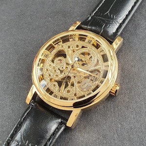 Relógio masculino automático de corda manual, mecanismo esqueleto, caixa dourada, pulseira de couro preta, estilo clássico para negócios e profissionalismo.