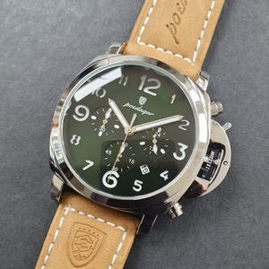 May include: A silver and green chronograph wristwatch with a brown leather band. The watch face has white numbers and hands, and the brand name "poedagar" is printed in white.