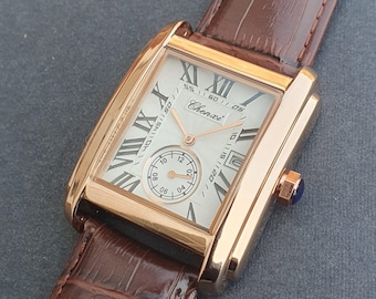 Puede incluir: Un reloj de pulsera rectangular dorado con una esfera clara, números romanos para las horas y un pequeño dial de segundos. El reloj tiene una correa de cuero marrón y la marca "Chenxi" es visible.