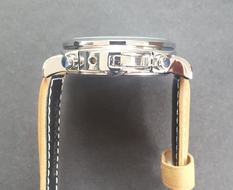 May include: A silver-toned wristwatch with a black leather band and a tan leather strap. The watch has a chronograph function and a date window.