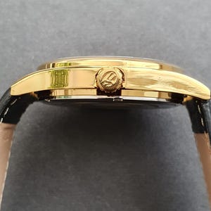 May include: A gold-tone wristwatch with a black leather band. The watch face is not visible in the image.