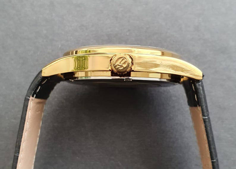 May include: A gold-tone wristwatch with a black leather band. The watch face is not visible in the image.