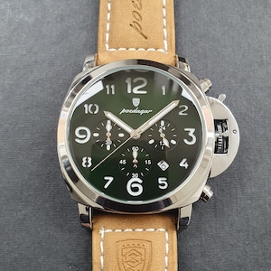 May include: A silver chronograph wristwatch with a green face and brown leather band. The watch face has white numbers and hands, and the brand name "poedagar" is printed in black.
