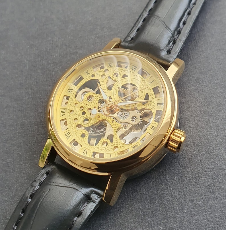 May include: A gold-toned skeleton watch with Roman numeral markings on the face and a black leather band.