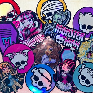 May include: A collection of Monster High stickers featuring various characters and logos. The stickers are holographic and have a variety of colors, including pink, purple, blue, and green. The stickers feature images of a coffin, a skull, a mirror, and various Monster High characters.