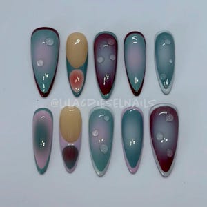 Puede incluir: Conjunto de diez uñas postizas largas en forma de almendra con un diseño degradado. Las uñas están pintadas en tonos de azul, rosa y blanco con puntos blancos en algunas uñas. Las uñas tienen una fina línea roja o blanca alrededor del borde.