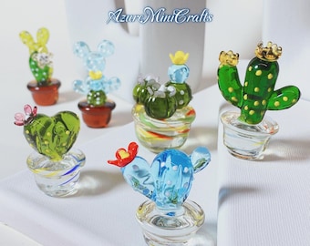 May include: A collection of miniature glass cactus sculptures in various colors, including green, blue, and yellow. Each cactus is potted in a small, clear glass pot. Some cacti have decorative elements like crowns and flowers. The text "Azure MiniCrafts" is visible.