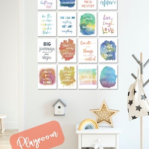 May include: A white wall with a collection of 12 colourful watercolour prints featuring inspirational quotes. The prints are arranged in a grid pattern and are framed with white borders. The wall is decorated with a small birdhouse and a rainbow-coloured wooden arch. A white bedside table with a drawer and a shelf is in the foreground. The bedside table is decorated with a wooden star, a rainbow-coloured wooden arch, and a white fabric bag with black stars. The text on the prints reads: "Believe you can and you're halfway there", "Every day is a new beginning. Take a deep breath and start again", "Done is better than perfect", "The world is a place to explore", "Be the reason someone smiles today", "You can do anything but not everything", "Smile more worry less", "Live, Laugh, Love", "Big journeys begin with small steps", "Start each day with a grateful heart", "Create the things you wish existed", "Just be you", "Enjoy the little things", "Create your own sunshine", "Do what makes you happy", "Learn something new today".