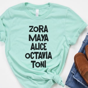 May include: A light green t-shirt with black text that reads "Zora Maya Alice Octavia Toni".