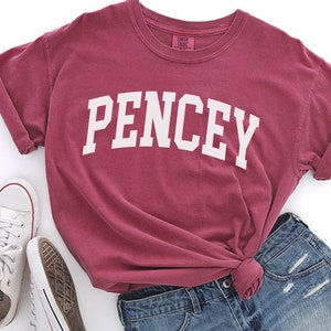 Könnte beinhalten: Ein maroonfarbenes T-Shirt mit dem Wort "PENCEY" in weiß auf der Vorderseite. Das Shirt ist aus weichem, bequemem Stoff und hat eine lockere Passform.