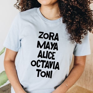 May include: A light blue t-shirt with black text that reads "Zora Maya Alice Octavia Toni".