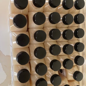 May include: A close-up view of a stack of 48 clear plastic bottles with black lids. The bottles are filled with a light-colored liquid.