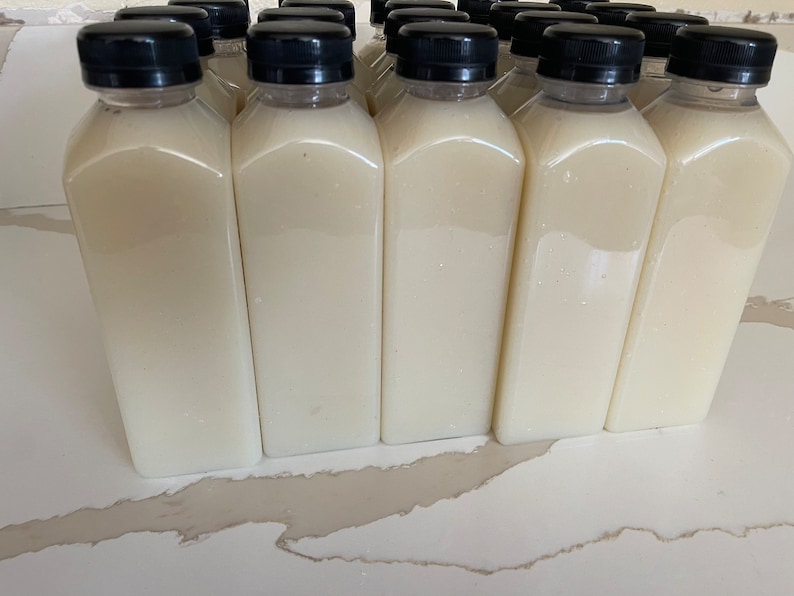 May include: A row of 10 clear plastic bottles with black lids filled with a white liquid. The bottles are arranged in a line on a white surface.