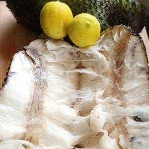 May include: A close-up of a split open soursop fruit with white flesh and two yellow limes on a wooden surface.