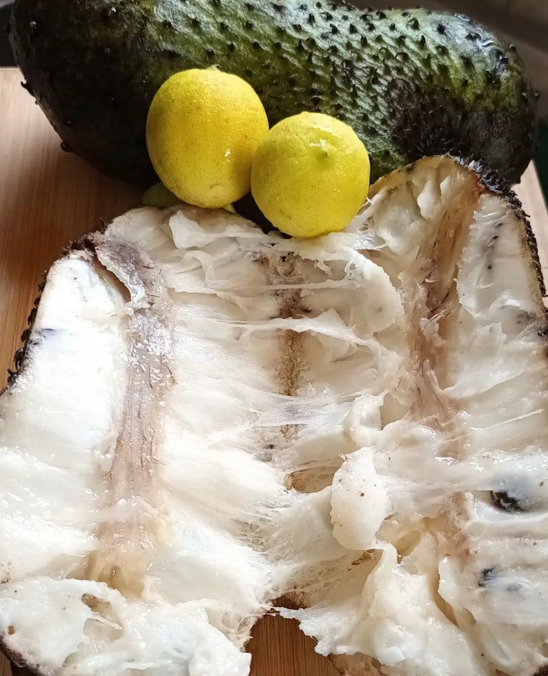 May include: A close-up of a split open soursop fruit with white flesh and two yellow limes on a wooden surface.