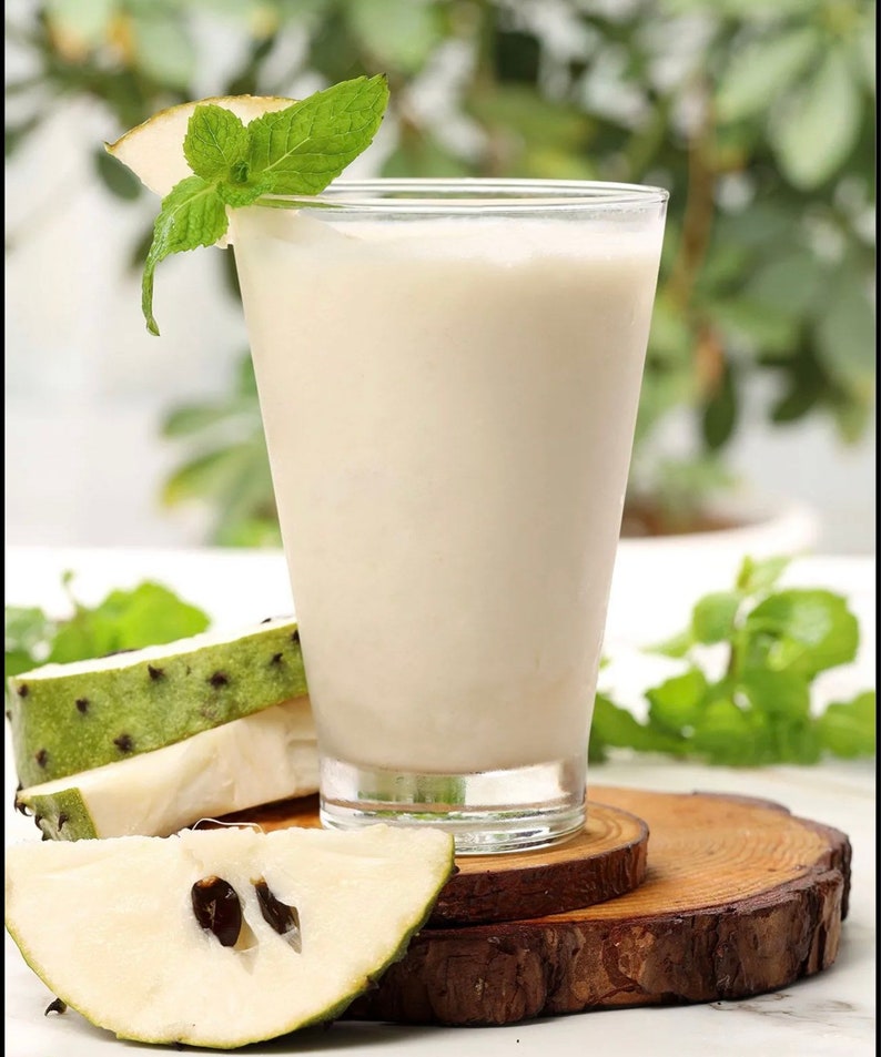 May include: A glass of creamy white smoothie with a sprig of mint on the rim, sitting on a wooden coaster with slices of green and white fruit.