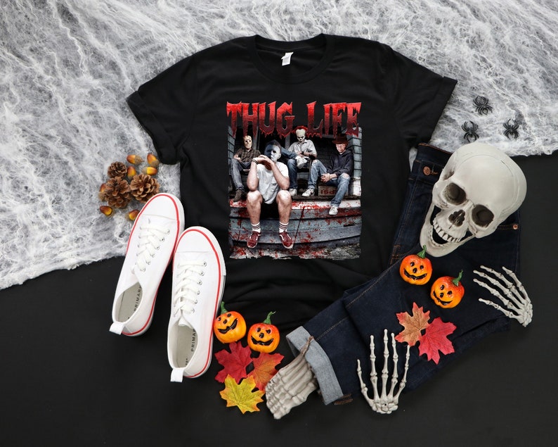 May include: Black t-shirt with the text "THUG LIFE" in red, featuring a graphic of four people. White trainers, blue jeans, a skull, and pumpkins are arranged around the shirt, creating a Halloween theme.