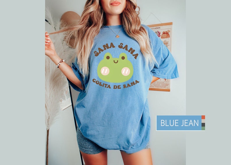 Puede incluir: Una camiseta azul de gran tama&ntilde;o con una rana de dibujos animados y el texto "Sana Sana Colita de Rana".
